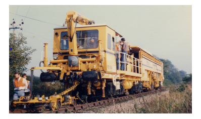 Stoneblower track-bed restoration machine on the rails, with Martin standing on the deck leaning against the railing.